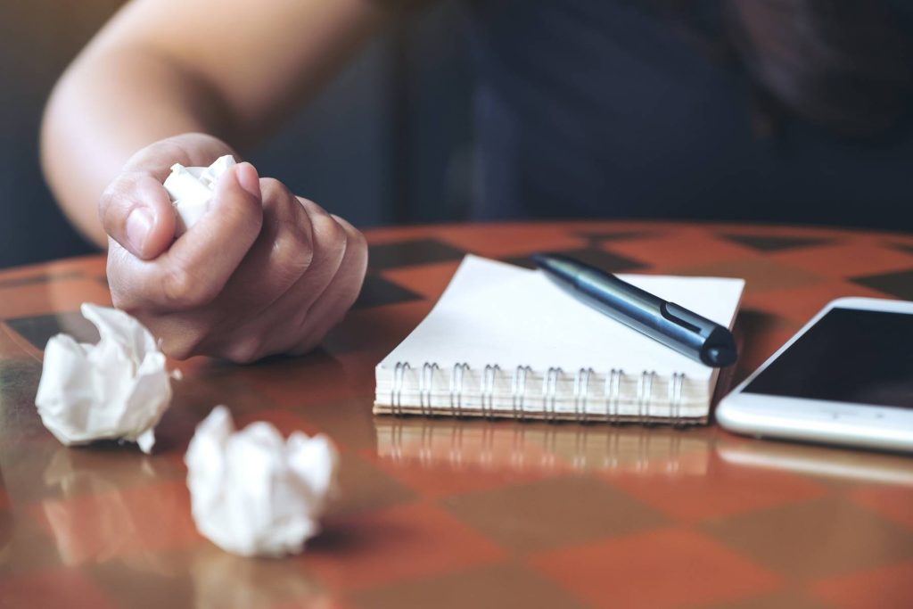 Clenched fist beside a notebook and crumpled paper on a desk